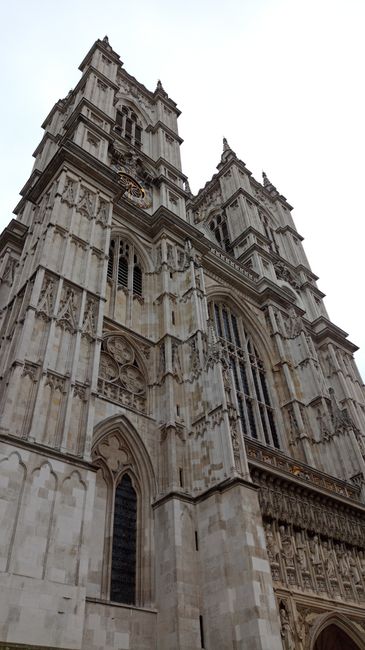A close-up view of the exterior of a historic Gothic-style cathedral, featuring tall pointed spires, ornate stone carvings, arched stained glass windows, and decorative pinnacles along the upper edges