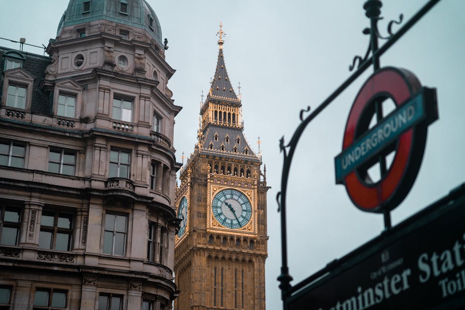 A close-up view of a London Underground sign hanging above a street entrance, with the iconic red circle and blue bar displaying the word 'UNDERGROUND'. The sign is mounted on a black metal bracket at